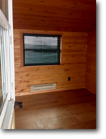 Cabin interior showing siding, flooring, heater and blinds.